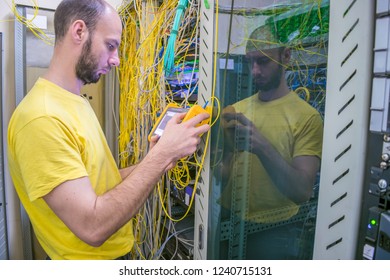 The system administrator is testing the network with a reflectometer.  The man works in the server room of the datacenter. A technician measures the signal level in a fiber optic cable. 