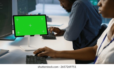 System administrator using isolated screen tablet, working in server farm to optimize it for data processing requirements. Software developer coding on chroma key device in data center, camera A