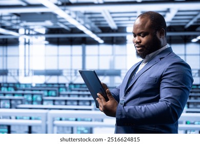 System administrator using tablet in data center with advanced tech, ensuring cybersecurity and efficient network management. Man in server hub optimizing data center equipment with device