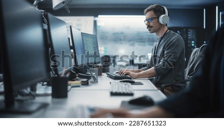 System Administrator Working in a Research E-Business Facility on a Desktop Computer. Focused Software Developer in Casual Clothes Wearing Headphones and Updating Server System Database