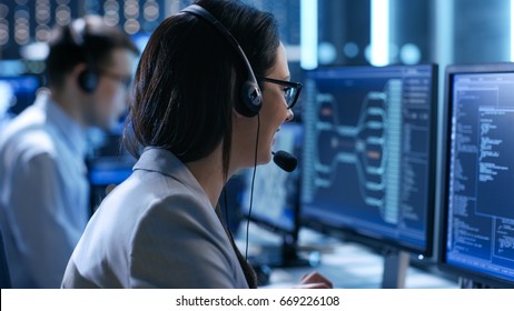 In The System Control Center Woman Working In A Technical Support Team Gives Instructions With The Help Of The Headsets. Possible Air Traffic/ Power Plant/ Security Room Theme.