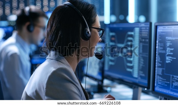 In the System\
Control Center Woman working in a Technical Support Team Gives\
Instructions with the Help of the Headsets. Possible Air Traffic/\
Power Plant/ Security Room\
Theme.