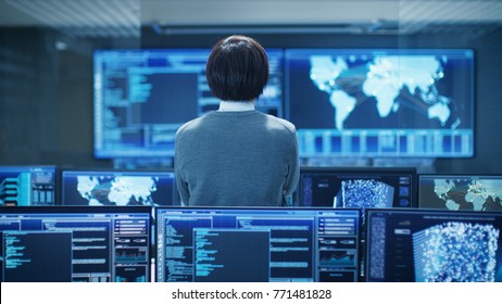 In The System Control Room Technical Operator Stands And Monitors Various Activities Showing On Multiple Displays With Graphics. Artificial Intelligence, Big Data Mining, Neural Network, Surveillance.