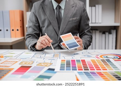 System Developer Analyzing UX UI Plans with Color Swatches and Design Layouts in a Modern Office Setting