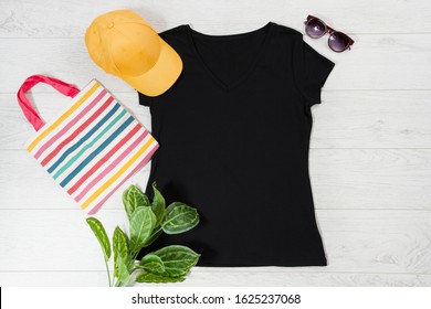 T Shirt Black. T-shirt Mockup Flat Lay With Summer Accessories. Baseball Hat, Bag And Sunglasses On Wooden Floor Background. Copy Space. Template Blank Canvas. Front Top View.