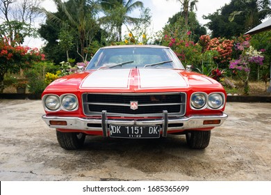 Tabanan, Bali / Indonesia - 29 February 2020: A Classic Red Muscle Car With Double White Strips, Named Holden Kingswood. Front View.