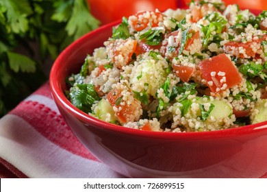 Tabbouleh salad with couscous in red bowl on rustic table
