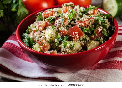 Tabbouleh salad with couscous in red bowl on rustic table