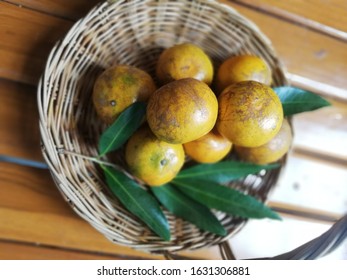 Tangerine​.A​  yellow​ fruit​ with​ green​ leaves​ in​ a​ wicker​ basket​ placed​ on​ a​  wooden​  table.