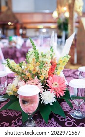Table Arrangement In A Wedding Party With Flower Bouquet And Glasses Of Water On Tablecloth With Bokeh Background. Selective Focus On Flower. No People.