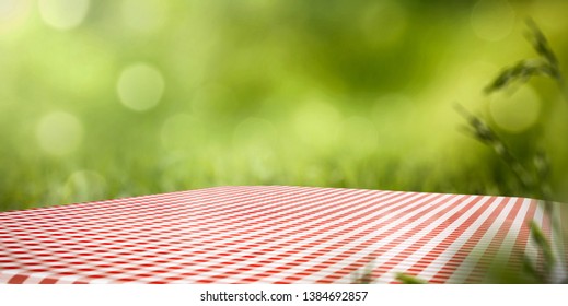 Table background of free space for your decoration. White and red tablecloth and green blurred background of grass and sun light. Summer time 