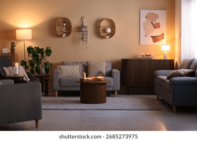 Table with burning candles, sofas and chest of drawers in interior of living room