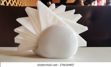 A Table In A Cafe And Restaurant. White Napkins In A Ceramic Napkin Holder. Hotel Dining Table With Napkins. A Paper Napkin Is Placed In A Glass On A Table In The Banquet Room.