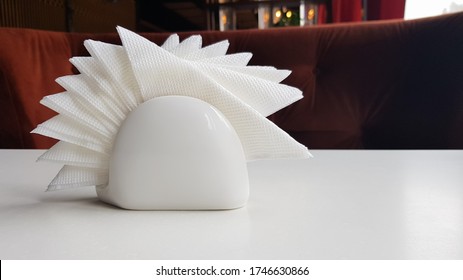 A Table In A Cafe And Restaurant. White Napkins In A Ceramic Napkin Holder. Hotel Dining Table With Napkins. A Paper Napkin Is Placed In A Glass On A Table In The Banquet Room.