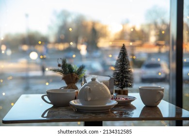 A Table In A Cafe With A View Of The Evening City. The Table Is Set For A Christmas Tea Party. Garlands Are Burning On The Window