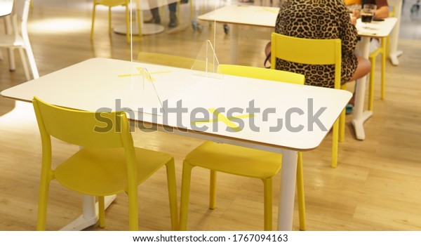 Table and chair arrangement with clear plastic\
barrier / divider on table with \'No seating\' sticker as part of\
safety protection for customers. New normal & Social\
distancing during Covid-19\
pandemic