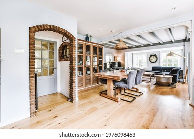 Table With Chairs Located Near Cupboard And Arched Doorway Decorated With Bricks In Dining Room At Home