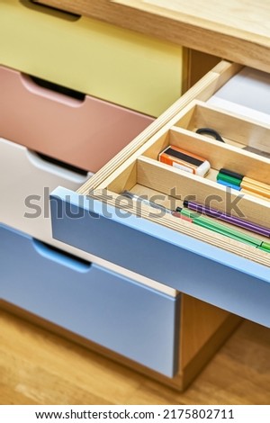 Table for children with multi-colored facades of roll-out drawers for stationery. Sawhorse desk made of plywood and solid oak close view