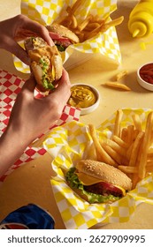 Table composition in warm yellow tones with junk food - hamburgers, wrapped in plain napkins, french fries, curry sauce and ketchup, and hands holding a half eaten burger. Close up image of food photo
