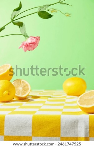 A table covered by a yellow checkered tablecloth containing some fresh yellow lemon above on light green background, a pink eustoma branch decorated. Blank space on table for showing product