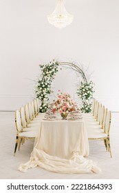 Table decorated for a wedding celebration. Bouquets of pink, white and peach flowers, vintage decor. White bright room, an arch of rose flowers