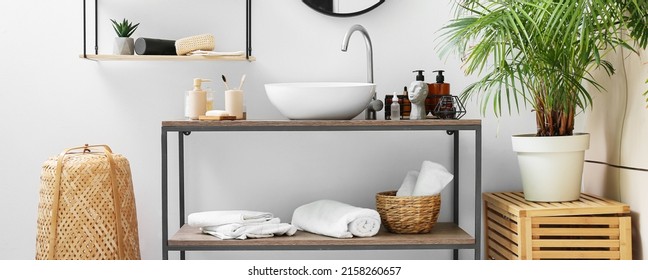 Table with different bath accessories and modern sink near light wall
