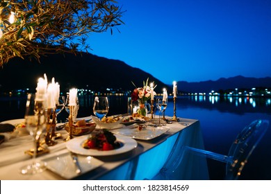 A table with dinner for two, a bouquet of flowers and candles against the backdrop of water and mountains in the evening, in a restaurant in the city of Kotor, Montenegro.