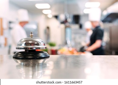 Table distribution in the restaurant. Cooks prepare food in the kitchen against the background of a metal bell - Powered by Shutterstock