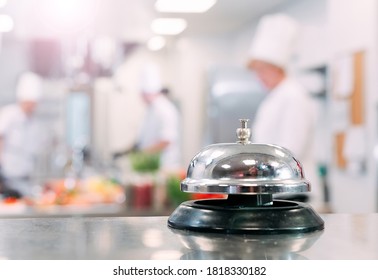 Table distribution in the restaurant. Cooks prepare food in the kitchen against the background of a metal bell