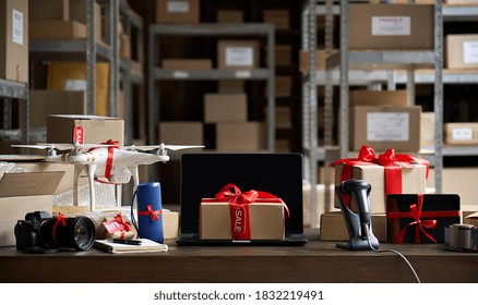 Table with electronic devices, laptop and gift box on table, warehouse storage background. Ecommerce gadgets store website discounts and gifts. Black friday and cyber monday best buy offers concept. - Powered by Shutterstock