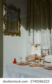 A table features plates, a doll, flowers, and a mirror in a well-lit room. It shows preparations for a celebration.