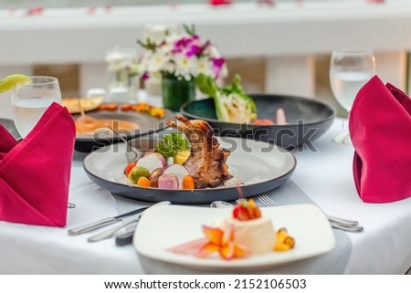 Table with fine food and drinks served for romantic dinner for couple, decorated with flowers and rose petals in luxury outdoors restaurant at hotel or resort. Summer vacations or holidays concept.