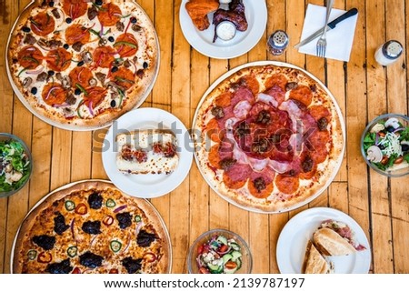 Table flat lay food collage of pizza , meatball sandwich , salad , calzones as well as buffalo and barbecue wings on a wooden background. 