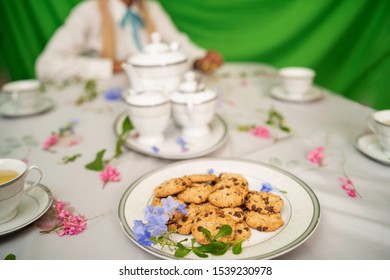 Table with a floral cover and a plate of chocolate biscuits or oatmeal cookies and a set of tea with green background.