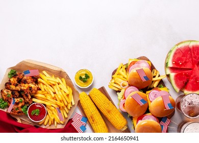 Table With Food For USA 4th July Independence Day. Fourth July Party Or Picnic Food With Burgers, Chicken Wings, Corn, Fries And Beer, Decorated With American Flags, Top View, Copy Space