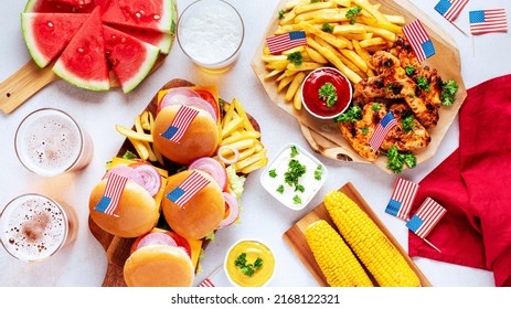 Table with food for USA 4th July Independence Day. Fourth July party or picnic food with burgers, chicken wings, corn, fries and beer, decorated with american flags, top view, copy space - Powered by Shutterstock