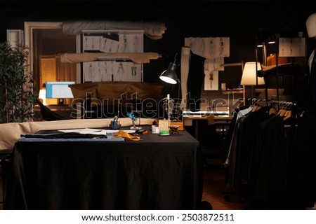 Table full of professional tailoring instruments used for manufacturing bespoke sartorial attire. Sewing machine, pins, needles, thread spools on table in atelier studio workspace