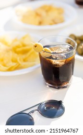Table full of snacks and a glass of vermuth during a sunny day. Chips, olives and vermut outside with sunglasses on a table.