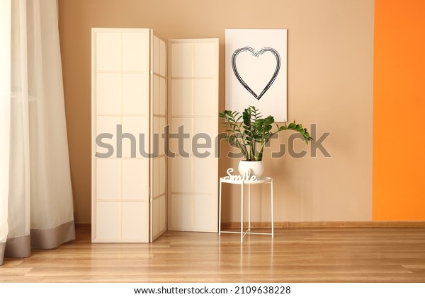 Table\
with houseplant and folding screen near beige\
wall