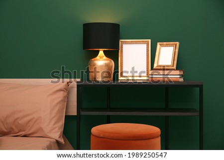 Table with lamp, books and empty frames near bed indoors. Interior design