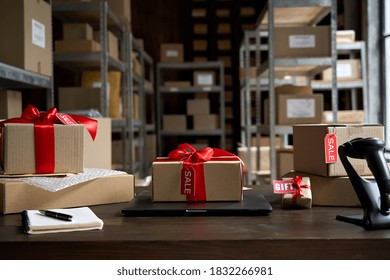 Table with laptop and gift boxes with sale tags on table in warehouse. Online ecommerce retail business black friday discounts deals, free shipping. Best buy holiday offers concept storage background.