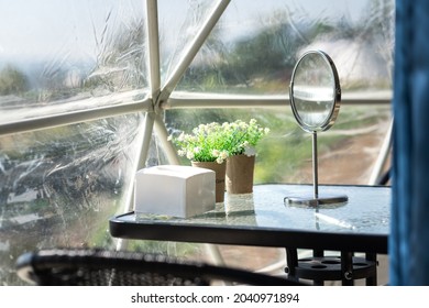 A Table In Living Room, Contained With Tissue Paper Box, Flower Pot,  Makeup Mirror And Opaque Plastic Canvas As Wall Structure. Interior Decoration And Object Photo.