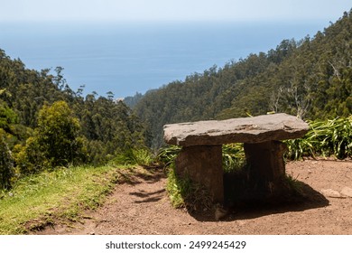 Table made of natural structured stone. Enligted by sunlight. View to a valley, covered by trees. Blue water of Atlantic ocean in the background. Levada das 25 fontes  Rabacal, Paul da Serra, Madeira.