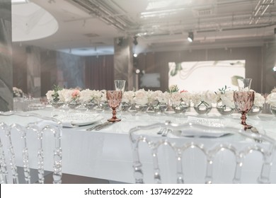 The table of the newlyweds. Small flower arrangements in ball glass vases. Interior of restaurant for wedding dinner, ready for guests. Catering concept.