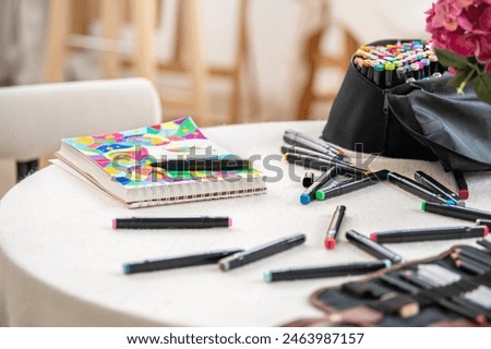 A table with a notebook and a bag of markers. The notebook is open to a page with a drawing of a unicorn