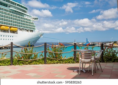 Table On Patio Of A Coastal Caribbean Restaurant With A Luxury Cruise Ship In The Background