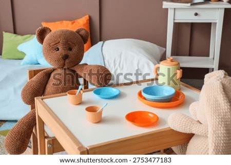 Table with plastic dishware and teddy bear in children's room, closeup