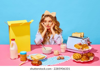 Table with products for breaksfast. Upset pretty girl in homewear and bow propping up cheeks sitting at table over light blue background. Concept of food, breakfast, vintage, retro, ad