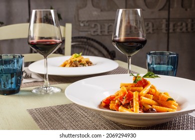 Table in a restaurant set with placemats, glasses for water, goblets with red wine and two first courses of pasta