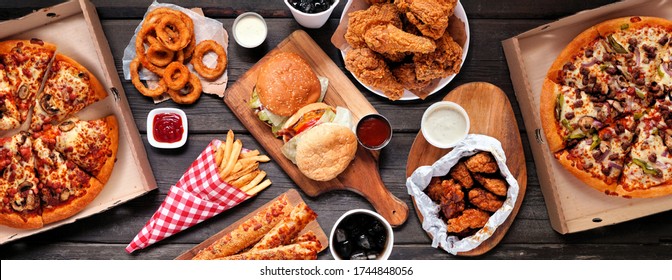 Table scene of assorted take out or delivery foods. Hamburgers, pizza, fried chicken and sides. Top down view on a dark wood banner background. - Shutterstock ID 1744848056
